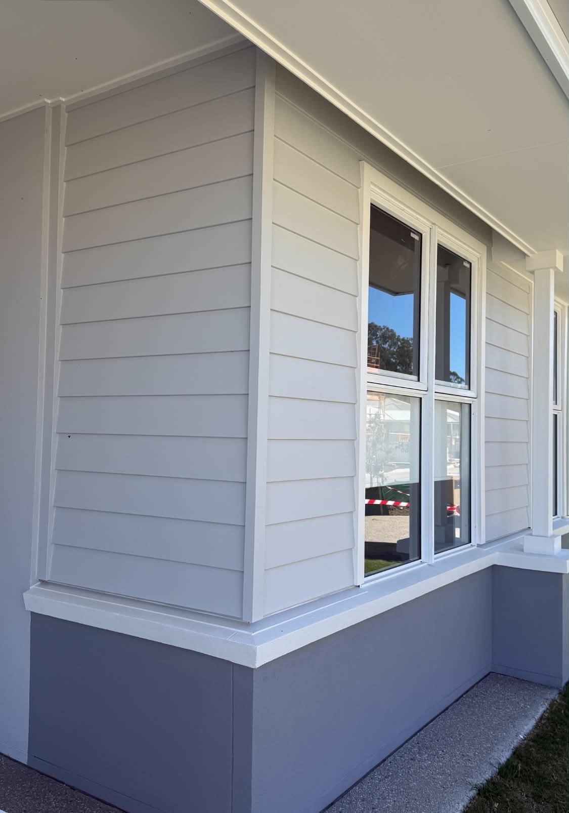 New build weatherboard cladding painted soft grey with white window surrounds and a darker base course