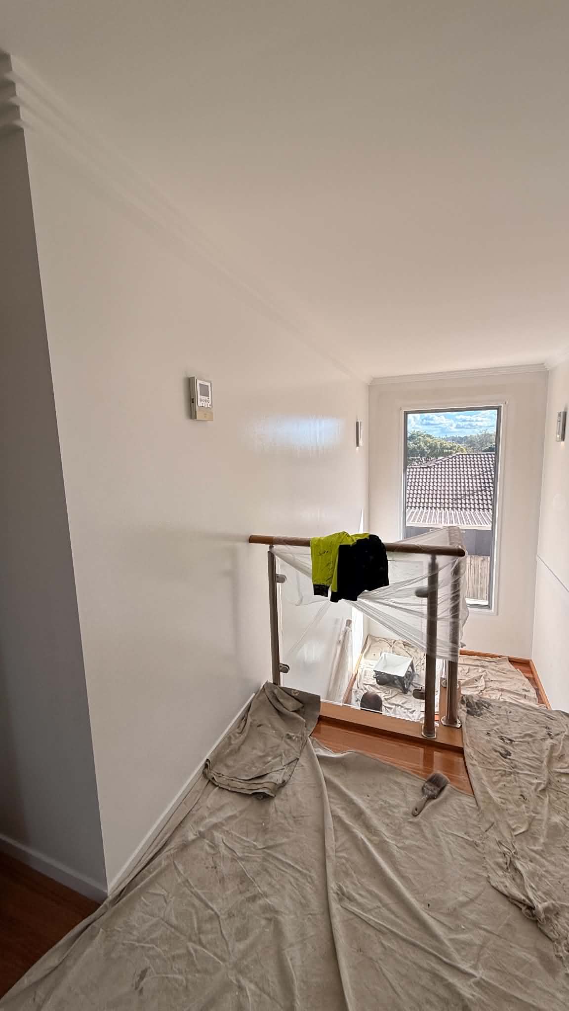 Upstairs landing painted white with canvas drop sheets and plastic sheeting protecting the glass balustrade