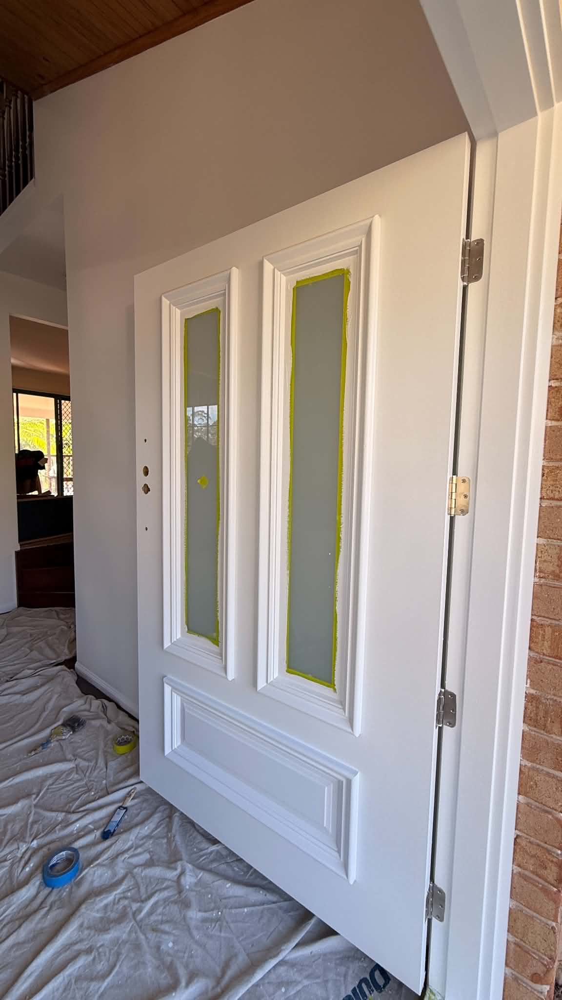 Panelled entry door finished in white enamel with glazed panels masked in tape